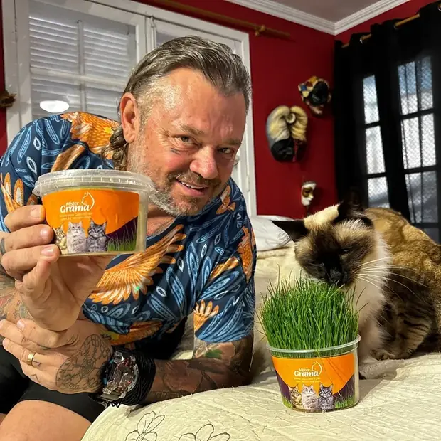 Richard Rasmussen segurando um pote de Mister Grama enquanto um gato come a grama do outro pote
